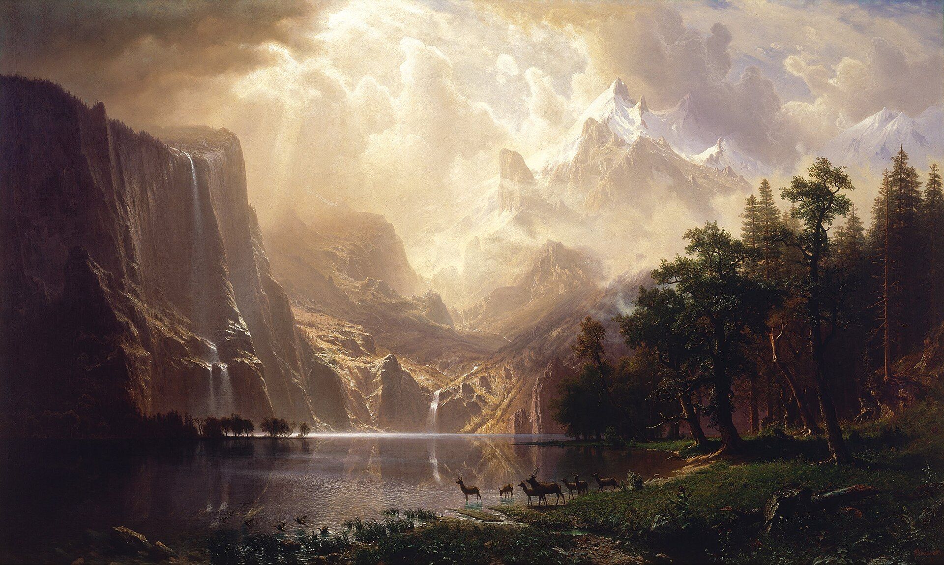 A still mountain lake with deer at its edge, waterfalls dropping from dark cliffs and snow peaks lit through a break in towering cloud