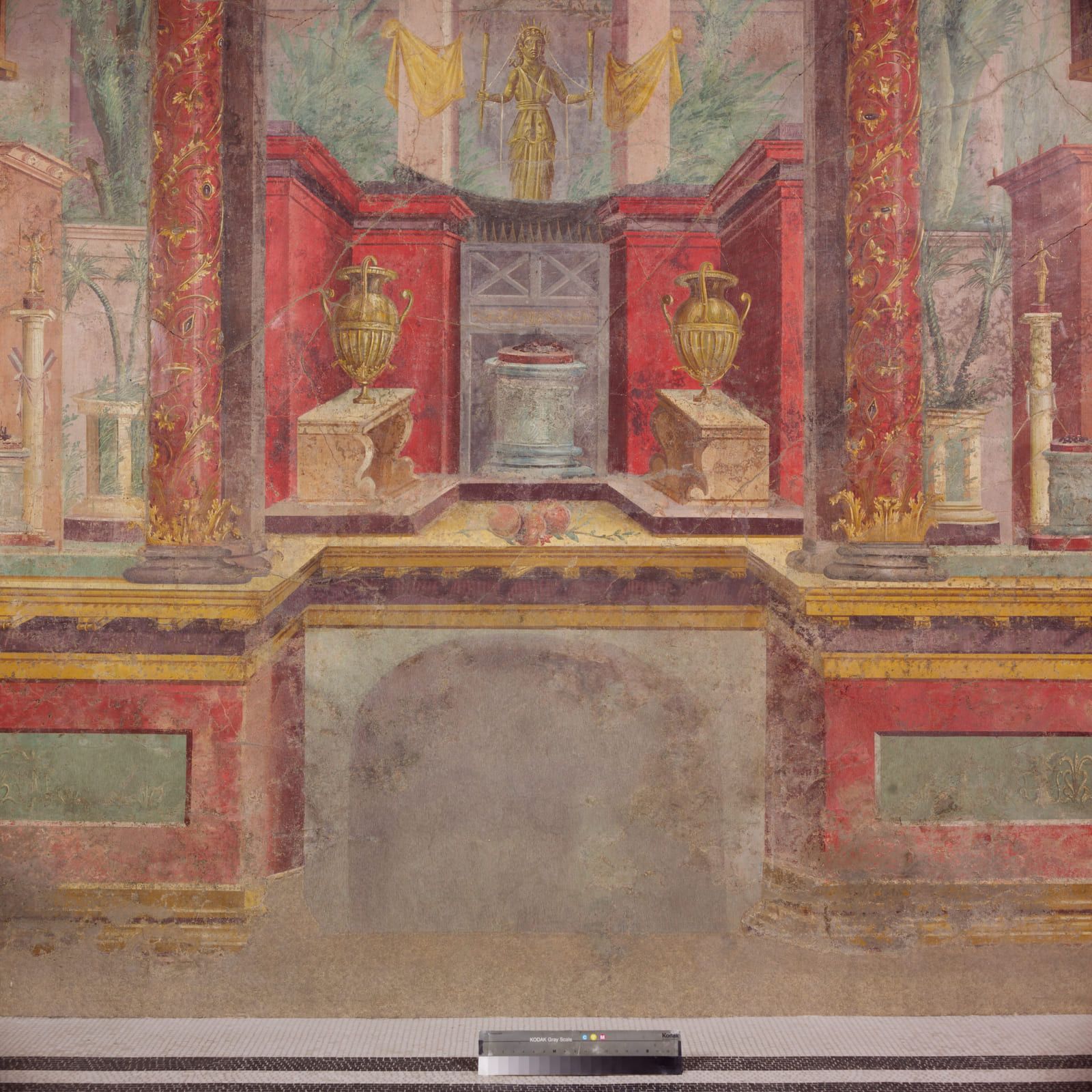 A red wall painted with columns, a shrine and a projecting cornice so the flat plaster reads as built architecture