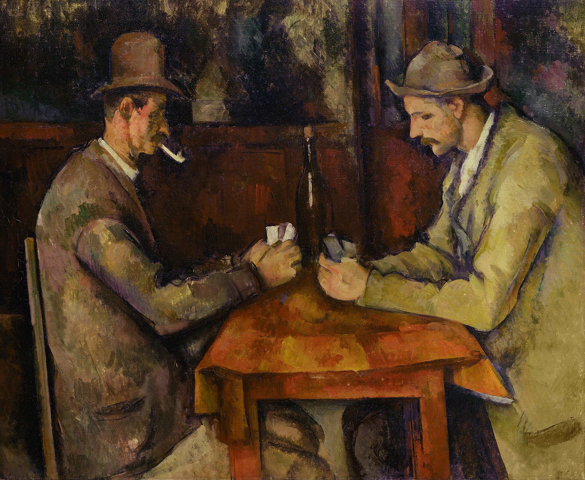 Two men in hats bent over their cards at a small table, a bottle standing between them against a plain brown wall