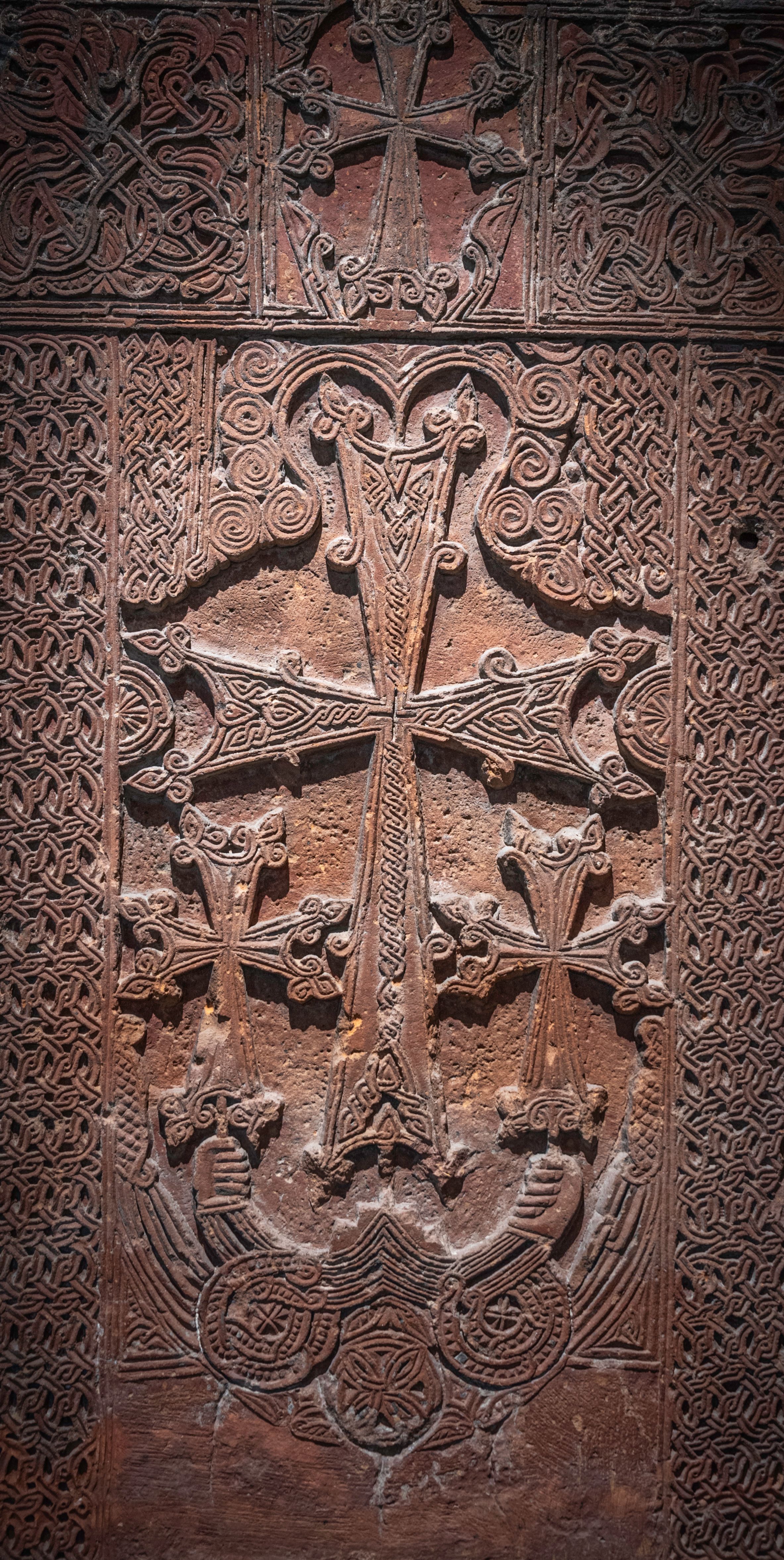 Carved brown stone filling the frame: a central winged cross over a rosette, two smaller crosses beside it, and broad borders of dense continuous interlace