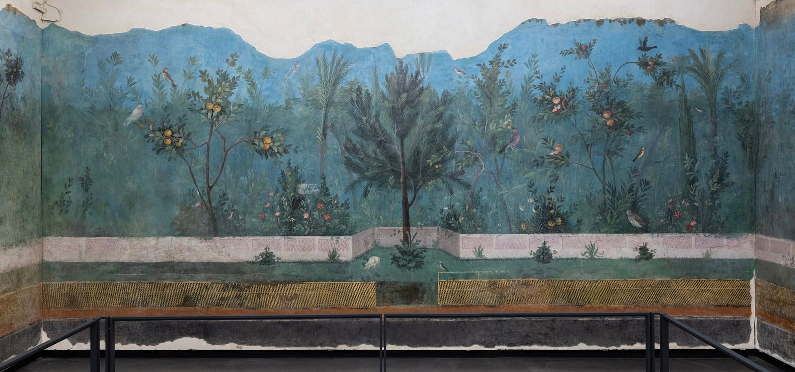 Fruit trees and small birds set against a blue-green sky above a low trellis fence, the whole wall painted as a garden