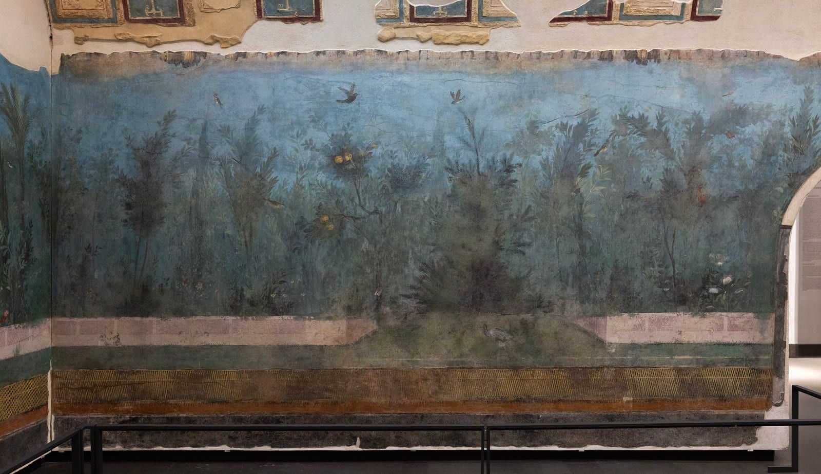 Two painted garden walls meeting at a corner, so the trees and fence carry round the angle without a break