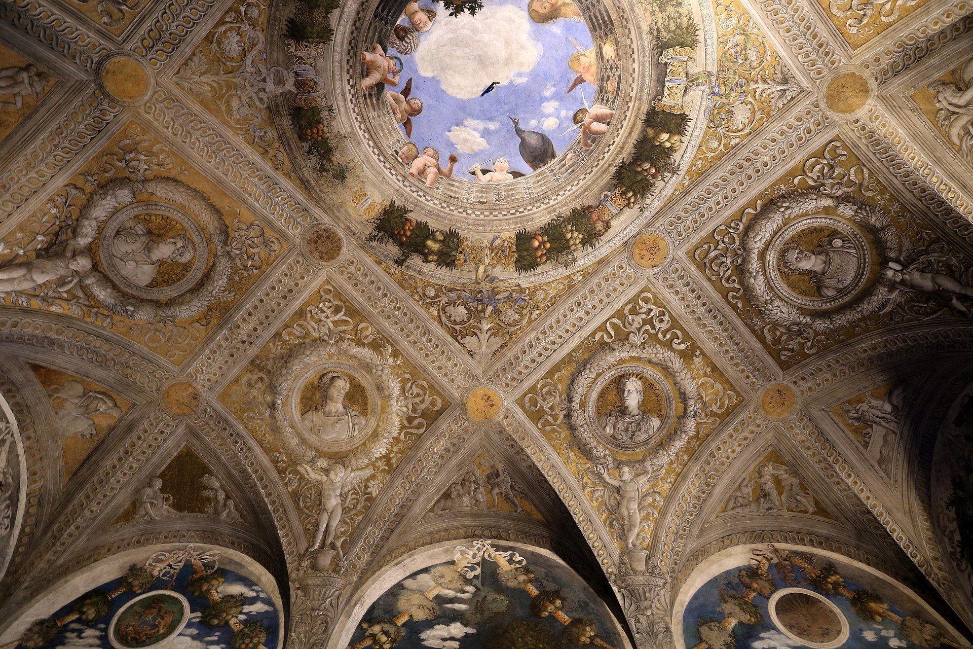 A painted vault of ribs, medallions and grisaille figures opening at its centre into a round balustrade with sky, cherubs and onlookers leaning over the edge