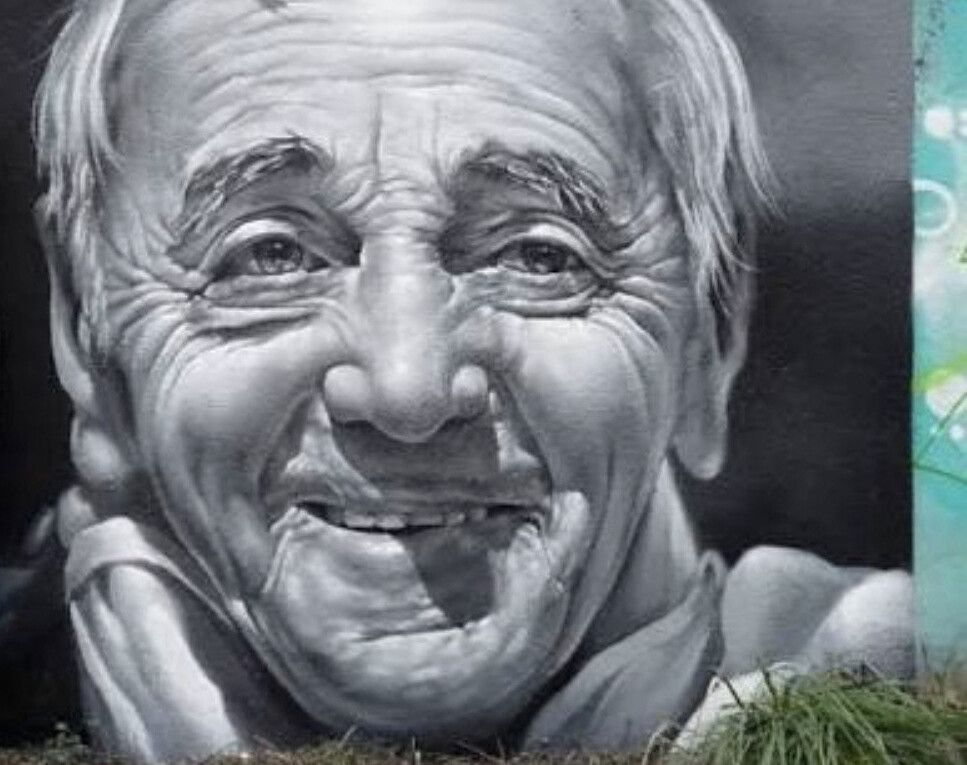 A laughing elderly man's face in grey and white filling a wall, deeply lined, the eyes almost closed