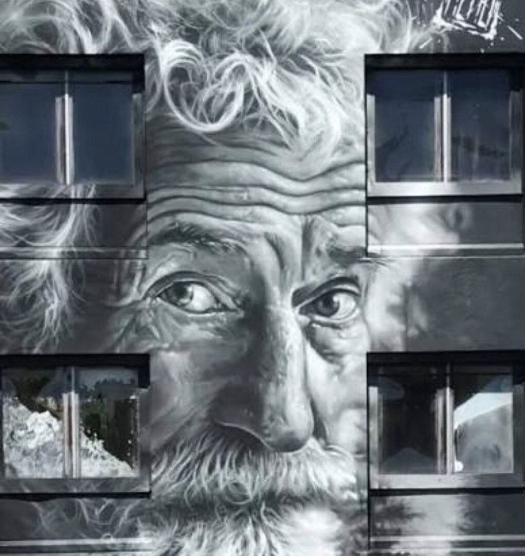 A bearded man's face in grey monochrome spread across the whole front of an apartment block, the building's windows falling inside the beard and brow