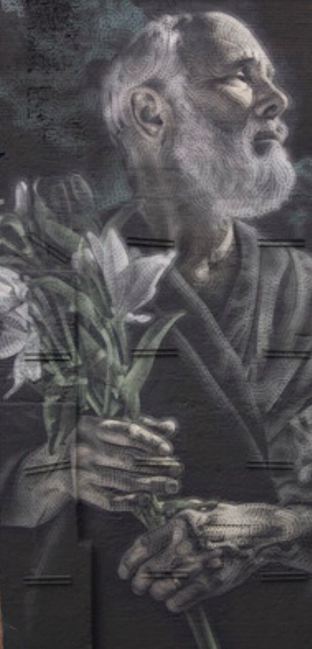 A white-bearded man looking upward and holding a bunch of lilies, drawn in pale grey the full height of a gable wall